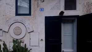 A building with a white facade, a black door, a small window, and a number '6' sign. - Casa della Luna (Matera)