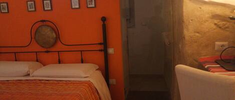 A bedroom with an orange headboard, a bed with a striped blanket, a white chair, and a small window.
