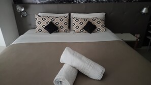 A neatly made bed with a brown bedspread and two patterned pillows, a white towel, and a nightstand with a lamp. - IQ Recoleta Plaza by Rapport Diseño in Recoleta, across from Plaza Vicente López   (Buenos Aires)