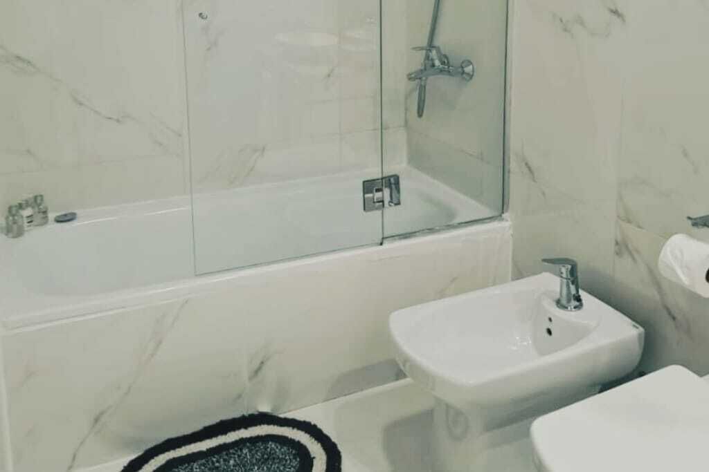 Een badkamer met een glazen douchecabine, een wit wastafelmeubel en een toilet.