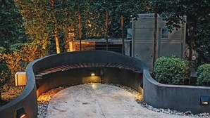 Ein geschwungener Betonweg mit einer Bank, umgeben von Grünpflanzen und einem Gebäude mit Außenbeleuchtung.