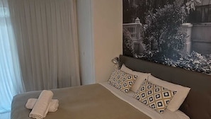 Ein Schlafzimmer mit Bett, Kopfteil, einem Fenster mit Vorhängen und einem an der Wand hängenden Bild.