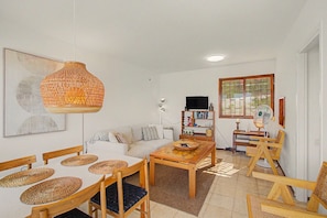 A living room with a sofa, coffee table, chairs, a hanging light fixture, a bookshelf, and a window with blinds. - ‘A La Playa in San Agustín’ with Sea Views, Private Terrace, and Wi-Fi (San Bartolomé de Tirajana)