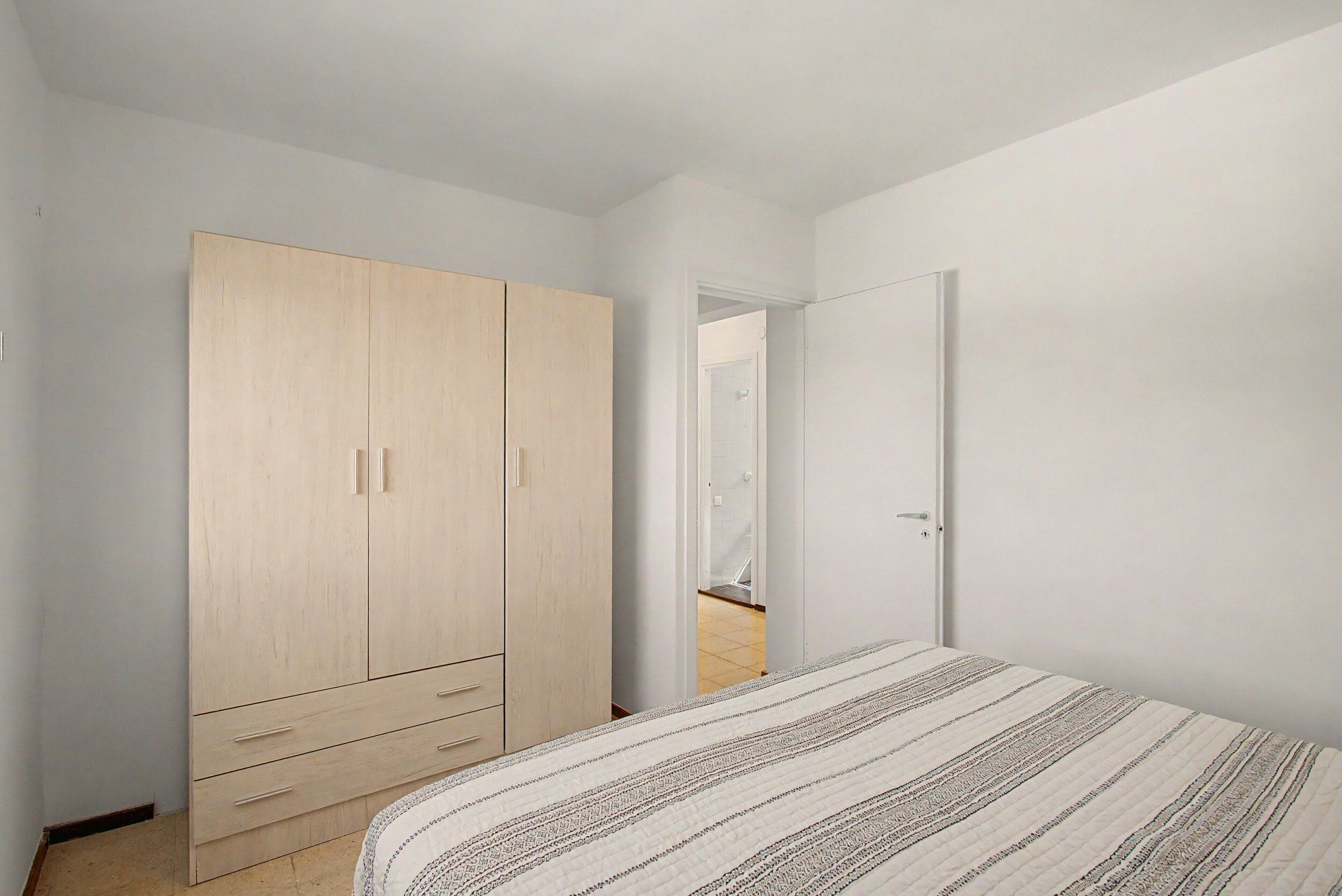 Une chambre à coucher comprenant un lit, une armoire et une porte donnant sur une autre pièce.