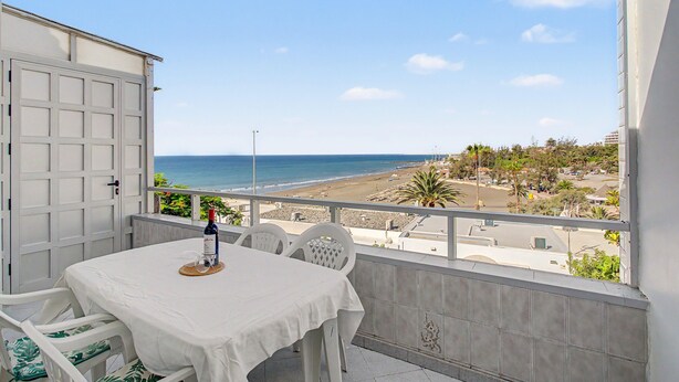 Un balcon avec une table et des chaises, donnant sur une plage et un quartier résidentiel.