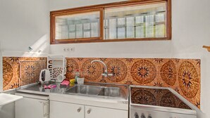 A compact kitchen with a sink, a kettle, and a stove.