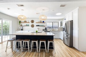 Una cocina moderna con una isla grande, taburetes de bar, un refrigerador y luces colgantes.