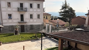 Une cour où une personne se détend sur une chaise, un bâtiment avec un toit en tuiles et une vue sur des montagnes lointaines.