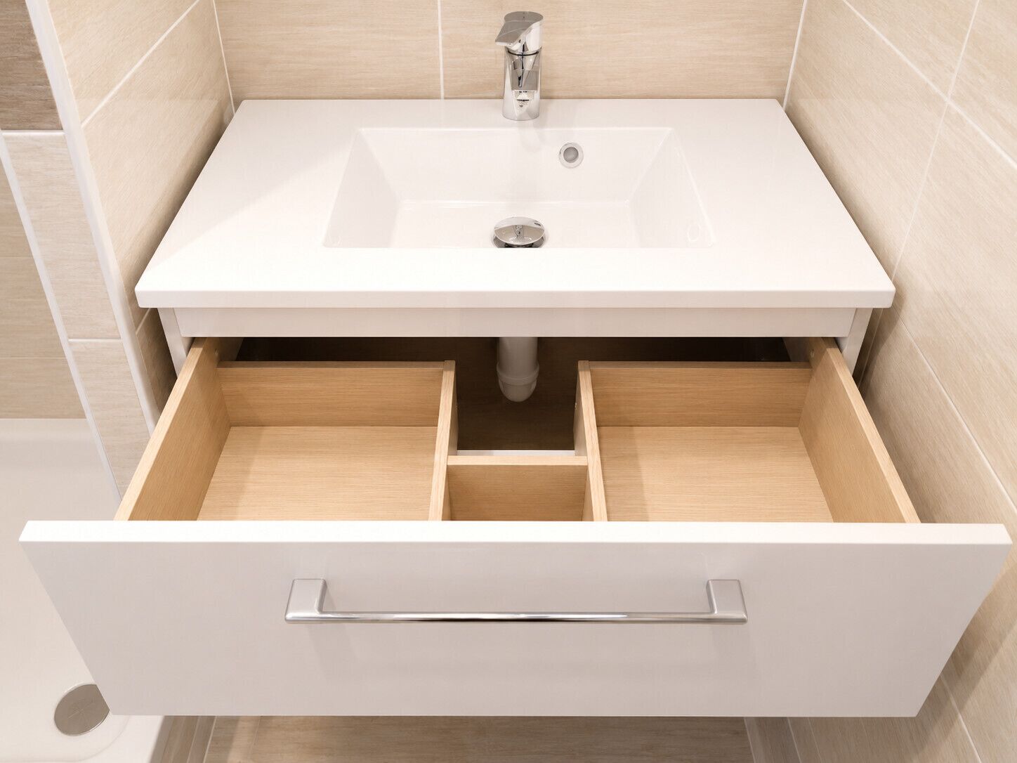 A bathroom with a white sink, a mirror, and a drawer with a silver handle.