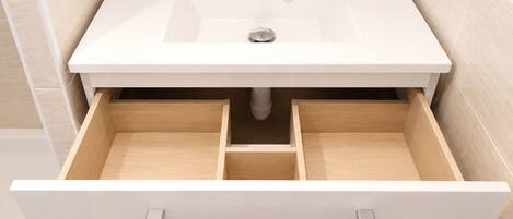 A bathroom with a white sink, a mirror, and a drawer with a silver handle.