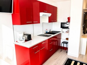 A modern kitchen with red cabinets, a white countertop, a coffee maker, a toaster, a sink, and a microwave. - Naturiste Cap d'Agde Port Vénus 324 (Agde)