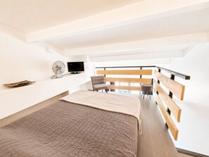 A modern bedroom with a bed, a chair, a TV, and a fan. - Naturiste Cap d'Agde Port Soleil 590 (Cap d'Agde)