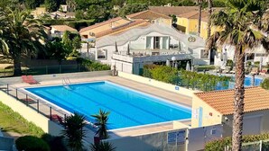 A swimming pool with a white fence, palm trees, and a hotel building in the background. - Naturiste Cap d'Agde Port Soleil 590 (Cap d'Agde)