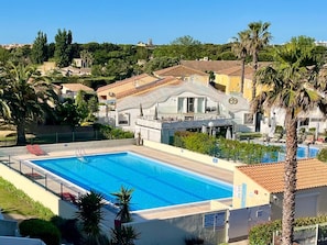 A swimming pool with a white fence, palm trees, and a hotel building in the background. - Naturiste Cap d'Agde Port Soleil 590 (Cap d'Agde)