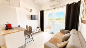 A modern living room with a sofa, a small table, a TV, and a balcony with curtains. - Naturiste Cap d'Agde Port Soleil 590 (Cap d'Agde)