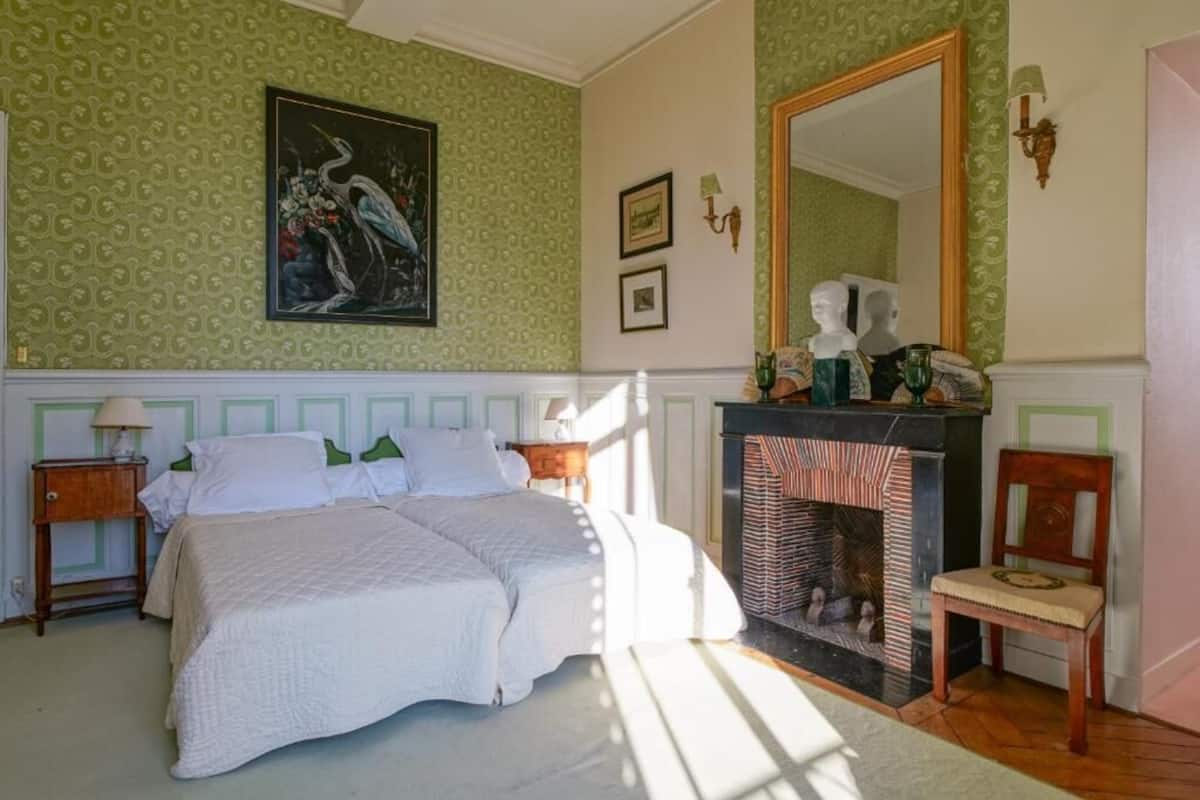 Un dormitorio con cama, chimenea, espejo y un cuadro en la pared.