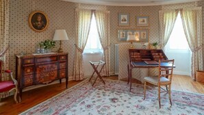 Una habitación con papel tapiz estampado, un aparador de madera, una silla roja, un escritorio de madera y una butaca con cojín.