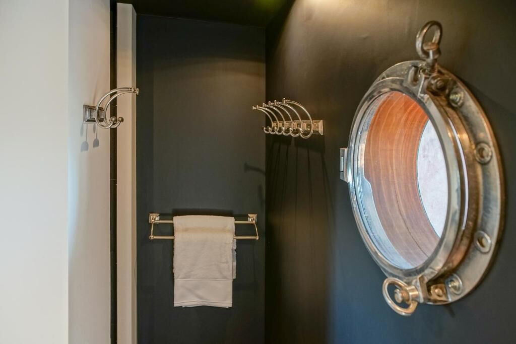 A bathroom with a dark wall, a towel rack, and a ship's wheel mirror.