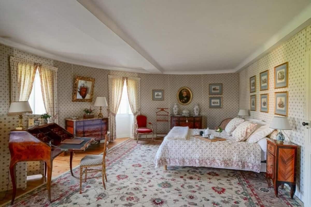 Un dormitorio con cama, escritorio, silla, cómoda y un sillón rojo.