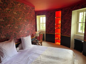 Habitación de hotel con cama, mesita de noche, lámpara, sillón, ventana y estante iluminado con luz roja.