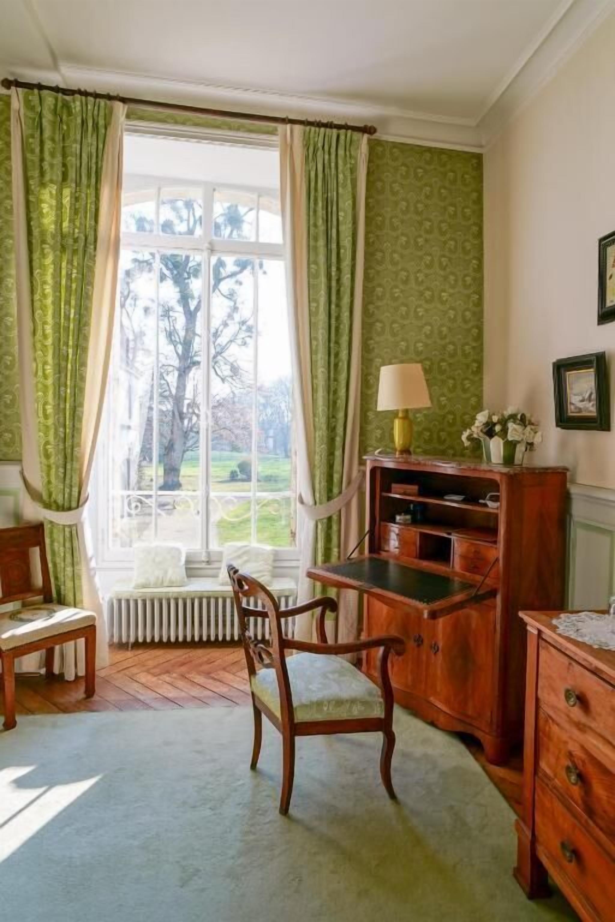 Une pièce avec une fenêtre, un bureau, une chaise, un radiateur et une lampe.