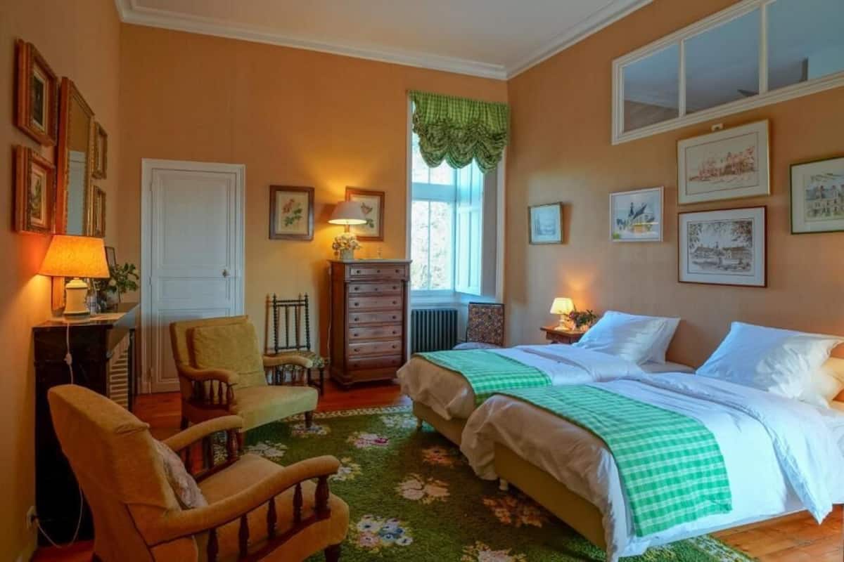 Un dormitorio con dos camas, una silla, un tocador y una ventana con un dosel verde.