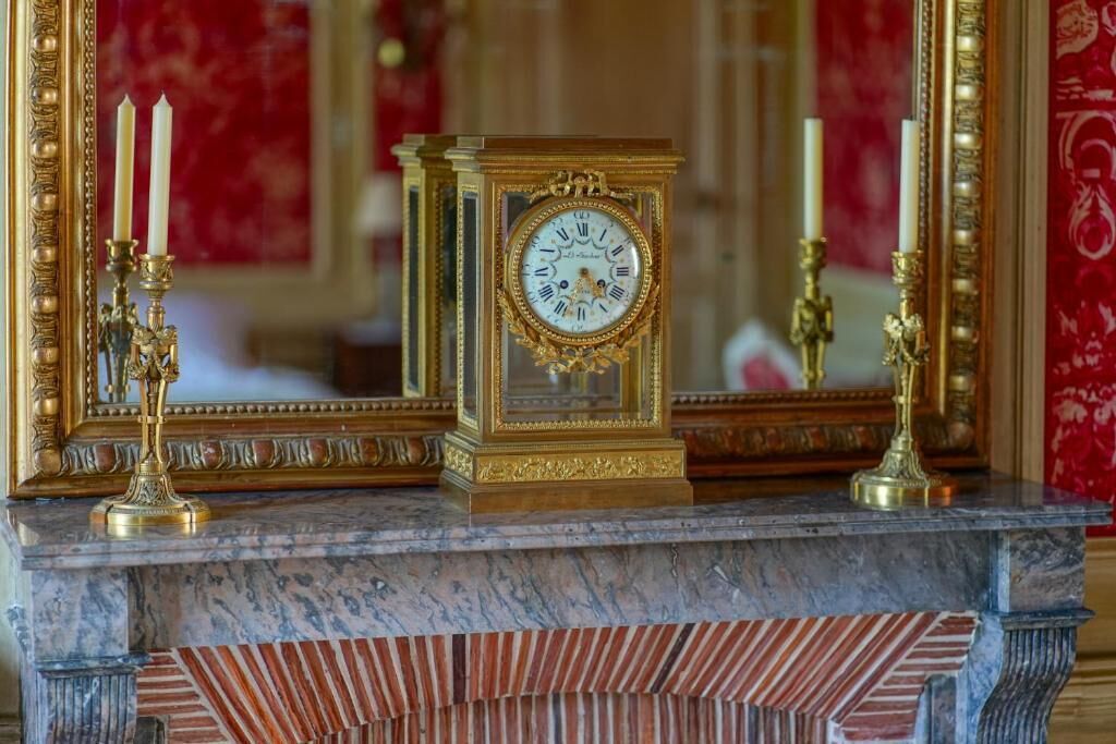 A marble fireplace with a decorative clock and candle holders.