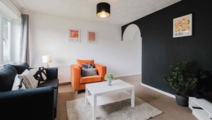 En stue med en sort sofa, en orange lænestol, et hvidt sofabord og en potteplante.