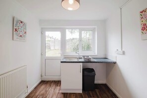 A small kitchen with a window, white cabinets, a black trash bin, and a countertop. - Spacious 3 Bedroom Home With Free Parking (West Northamptonshire)