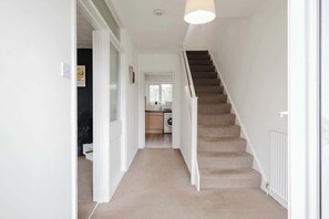 Ein Flur mit Teppichboden, eine Treppe mit beigefarbenen Stufen und eine weiße Tür zu einem Zimmer.