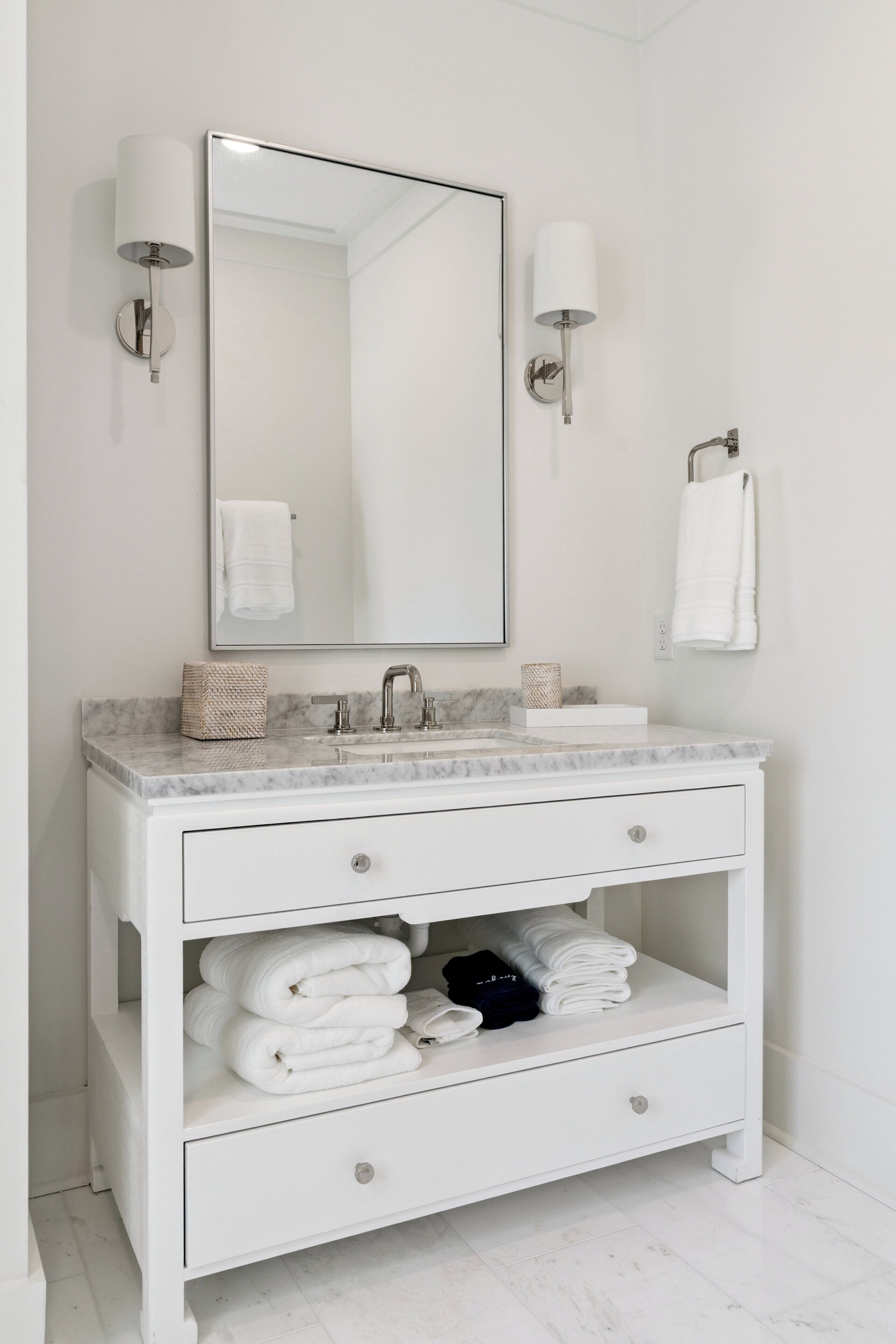 A white bathroom vanity with a marble countertop, a large mirror, two wall-mounted light fixtures, and a towel rack.