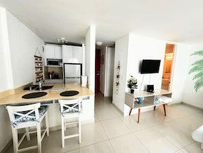 A modern kitchen with a central island, white cabinetry, and a flat-screen TV mounted on the wall. - Palmas Terrace Studio Breathtaking Ocean View (San Juan)