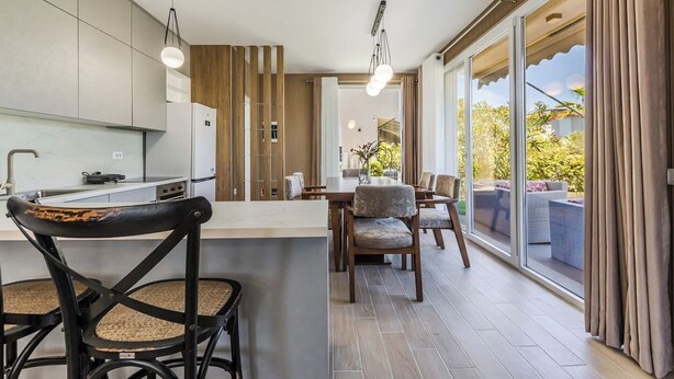 A modern kitchen with a dining area, large windows, and a view of the outdoors.