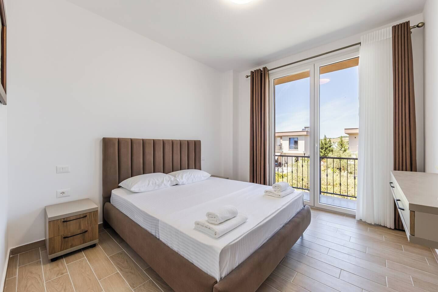 A bedroom with a bed, a nightstand, a desk, and a view of the outside.