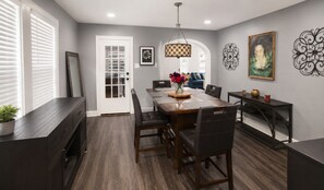 A dining area with a wooden table, chairs, a vase of flowers, and decorative wall art. - Houston Bungalow Near Sports, Downtown & Parks! (Houston)