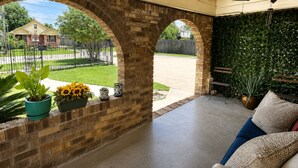 Un portico coperto con archi in mattoni, arredo da esterno, piante in vaso e vista su una strada residenziale.