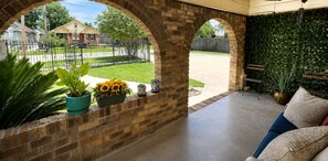 A covered patio with brick arches, outdoor seating, potted plants, and a view of a residential street. - Houston Bungalow Near Sports, Downtown & Parks! (Houston)