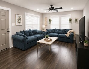 A modern living room with a sectional sofa, a coffee table, a ceiling fan, and a TV. - Houston Bungalow Near Sports, Downtown & Parks! (Houston)