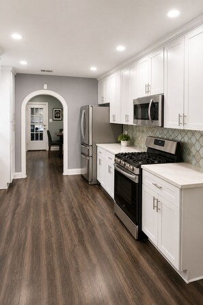A modern kitchen with white cabinetry, stainless steel appliances, and a dark wood floor. - Houston Bungalow Near Sports, Downtown & Parks! (Houston)