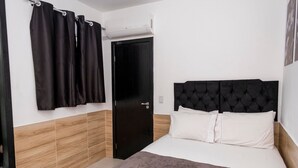 A bedroom with a bed, a black headboard, a door, and a window with curtains. - Comfort and tranquility near the airport (Vitória)