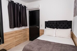 Ein Schlafzimmer mit einem Bett, einem schwarzen Kopfteil, einer Tür und einem Fenster mit Vorhängen.