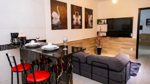 A modern kitchen with a dining area, a sofa, and a flat-screen TV mounted on the wall. - Comfort and tranquility near the airport (Vitória)