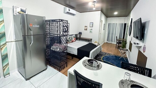 A compact hotel room with a kitchenette, a dining area, and a TV mounted on the wall. - Modern and functional studio apartment near Garoto (Vila Velha)