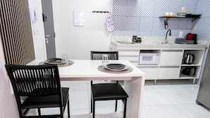 A compact kitchen with a microwave, kettle, and a small shelf with cups. - Modern and functional studio apartment near Garoto (Vila Velha)