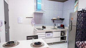 A compact kitchen with a microwave, kettle, and a gas stove. There is a dining table with plates and cutlery. - Modern and functional studio apartment near Garoto (Vila Velha)