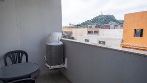 A balcony with a table and chairs, an air conditioning unit, and a view of buildings and a hill. - Modern and functional studio apartment near Garoto (Vila Velha)