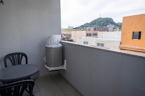 Ein Balkon mit Tisch und Stühlen, einer Klimaanlage und Blick auf Gebäude sowie eine Hügelkulisse.