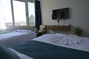 Quarto de hotel com duas camas, televisão, escrivaninha e janela com vista.