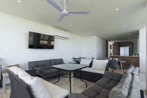 A modern living room with a flat-screen TV mounted on the wall, a ceiling fan, and a dining area with a table and chairs. - Beachfront Paradise with Shared Pool Telchac | Depto A12 (Telchac Puerto)