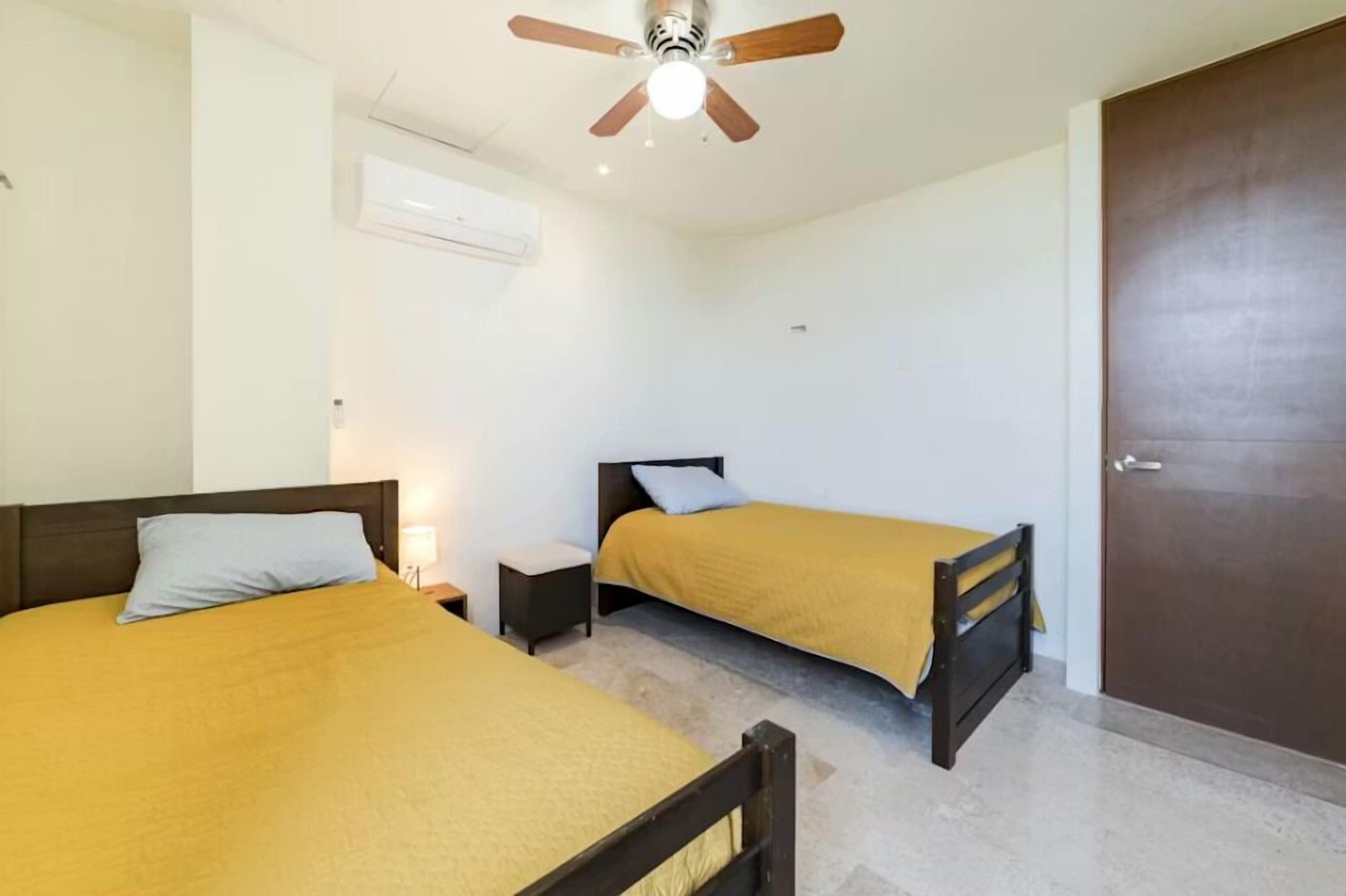 Une chambre avec deux lits, un ventilateur de plafond, un appareil de climatisation et une porte.